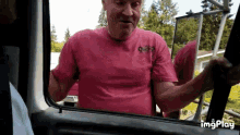 a man in a pink shirt is standing in a car looking out the window .