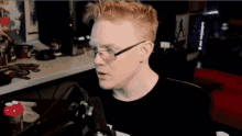 a man with glasses is sitting in front of a microphone with his mouth open