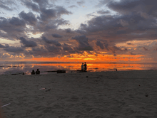 a couple standing on a beach watching a sunset