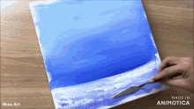 a person is painting a blue and white landscape on a canvas with the words wow art below it