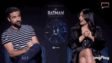 a man and woman sit in front of a batman poster