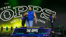 a man in a blue shirt is standing in front of a sign that says " the opps "