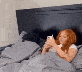 a woman with long red hair is laying in bed looking at her phone