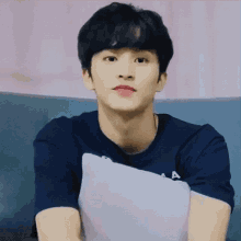 a young man in a blue shirt is sitting on a couch holding a pillow .