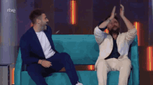 two men are sitting on a blue couch with their hands in the air and the letters rtve in the corner