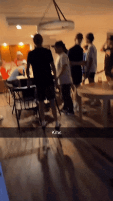 a group of people are gathered in a room with kms written on the bottom