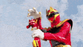 a red and gold power ranger is holding a red object in his hand .