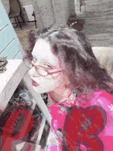 a woman wearing glasses and a pink shirt is standing in front of a shoe rack