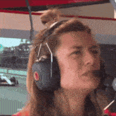a woman wearing headphones and a microphone looks at a race track