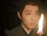 a man in a suit is holding a candle in his hand in the dark .