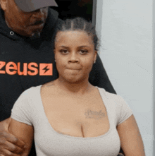 a woman with a tattoo on her chest is standing next to a man wearing a shirt that says zeus