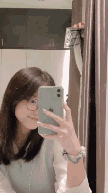 a woman is taking a selfie in front of a mirror with her iphone .