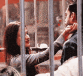 a woman is touching a man 's face behind bars with a clock in the background