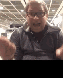 a man wearing glasses and a grey sweater is making a funny face .