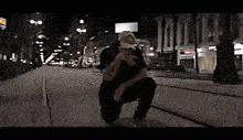 a man is kneeling down on a sidewalk in a city at night