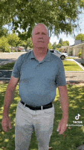 a man in a blue shirt and white pants is standing in a grassy field .