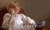 a woman is sitting in a chair talking on a cell phone and saying okay dokey .