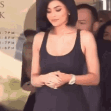 a woman in a black tank top is standing in front of a sign that says ' s k ' on it .