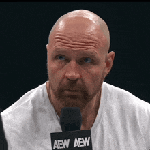 a bald man with a beard is wearing a white shirt and a microphone that says aew