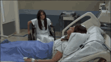 a woman in a hospital gown sits next to a woman in a wheelchair