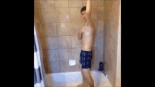 a shirtless man in blue boxer shorts is standing in a bathtub .