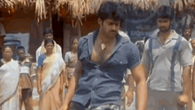 a man in a blue shirt is standing in front of a group of people in a village .