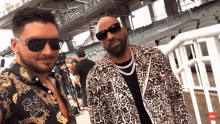 a man wearing sunglasses stands next to another man wearing a leopard print jacket