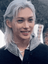 a young man with long white hair is smiling and wearing a necklace