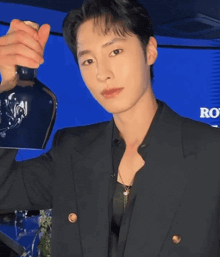 a young man in a black suit is holding a bottle