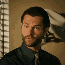 a man with a beard wearing a blue shirt and tie is looking at the camera