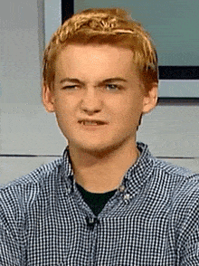 a young man wearing a plaid shirt making a funny face