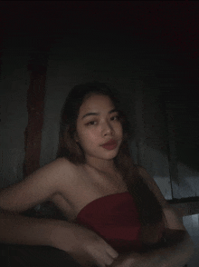 a woman in a red strapless top looks at the camera in a dark room