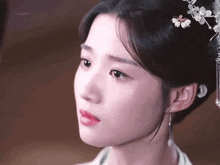 a close up of a woman 's face with a flower in her hair and a watermark that says ' gugubb '
