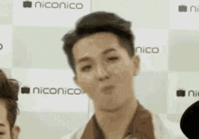 a close up of a man making a funny face in front of a niconico sign .