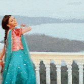 a woman in a blue and pink dress is standing on a balcony overlooking a body of water ..