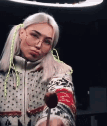 a girl wearing glasses and a sweater is holding a lollipop in her hand .