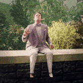a man in a suit and bow tie is sitting on a ledge