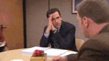 a man in a suit and tie is sitting at a table with another man