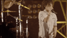 a man in a white shirt sings into a microphone on a stage