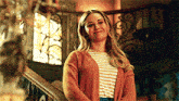 a woman is standing on a set of stairs wearing a striped shirt and an orange cardigan .
