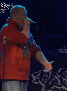 a man in a red hoodie sings into a microphone in front of a sign that says records.fi