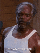 a man with a beard and a white tank top is standing in front of a building .