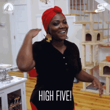 a woman wearing a red turban says high five in front of a cat tree