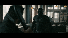 a man in a black suit holds a gun in front of another man in a black suit