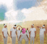 a group of men wearing white shirts and headbands are standing in a field with a man with a pink face and a halo