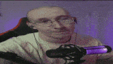 a bald man wearing glasses and earbuds is sitting in front of a microphone .