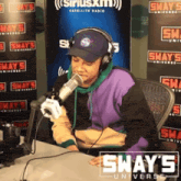 a man wearing headphones speaks into a microphone in front of a sign that says sway 's universe