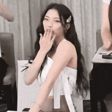 a woman with long hair is covering her mouth with her hand while standing in a room .
