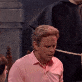 a man in a pink shirt sits in a chair with a rope around his neck