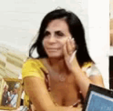 a woman in a yellow shirt is sitting at a table with her hands on her face and a book .